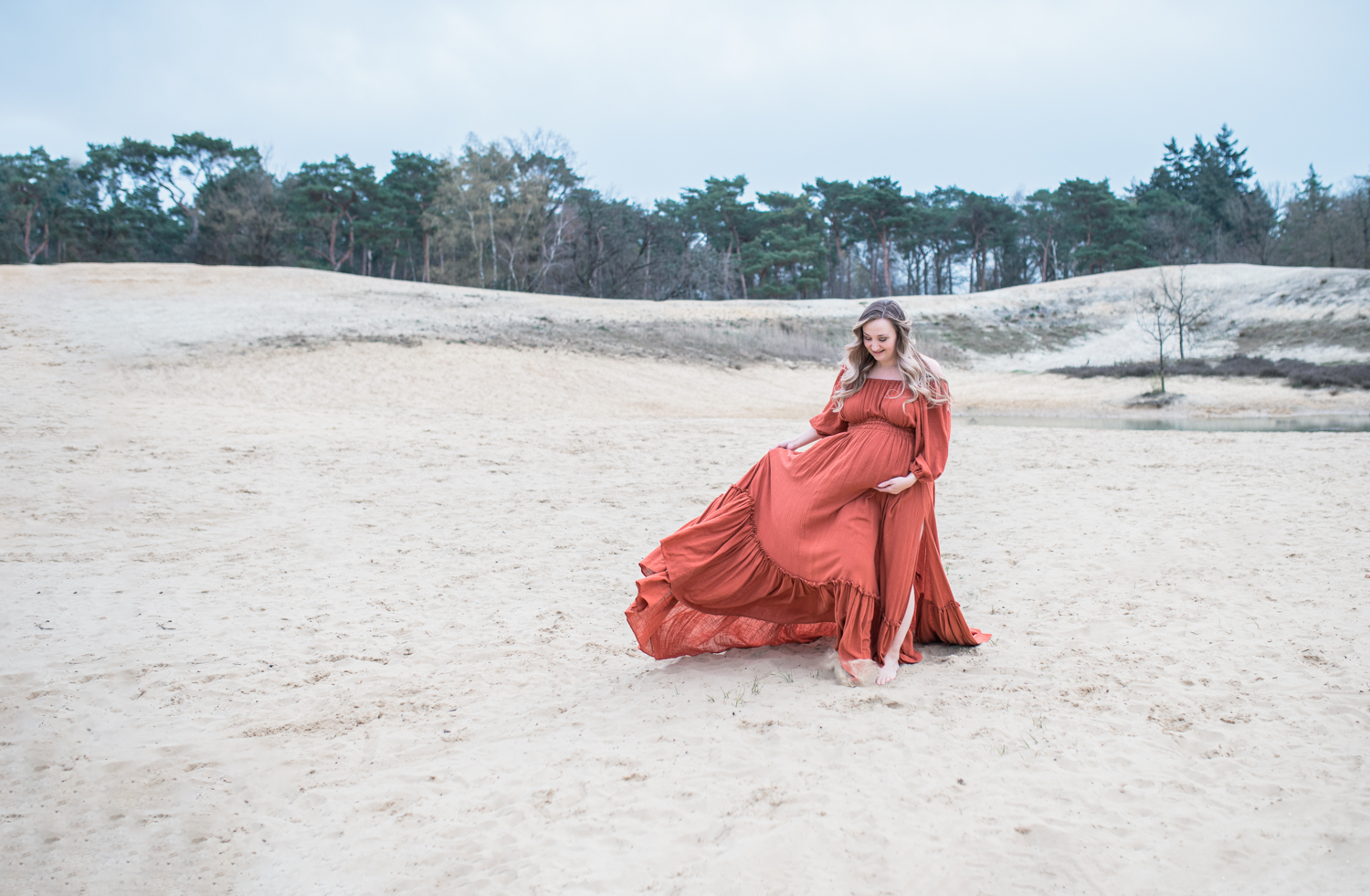 Puur Geluk Fotografie legt een zwangere vrouw vast in een vloeiende jurk op een lichte zandvlakte, rustig en natuurlijk gefotografeerd met aandacht voor zachtheid en verwachting.