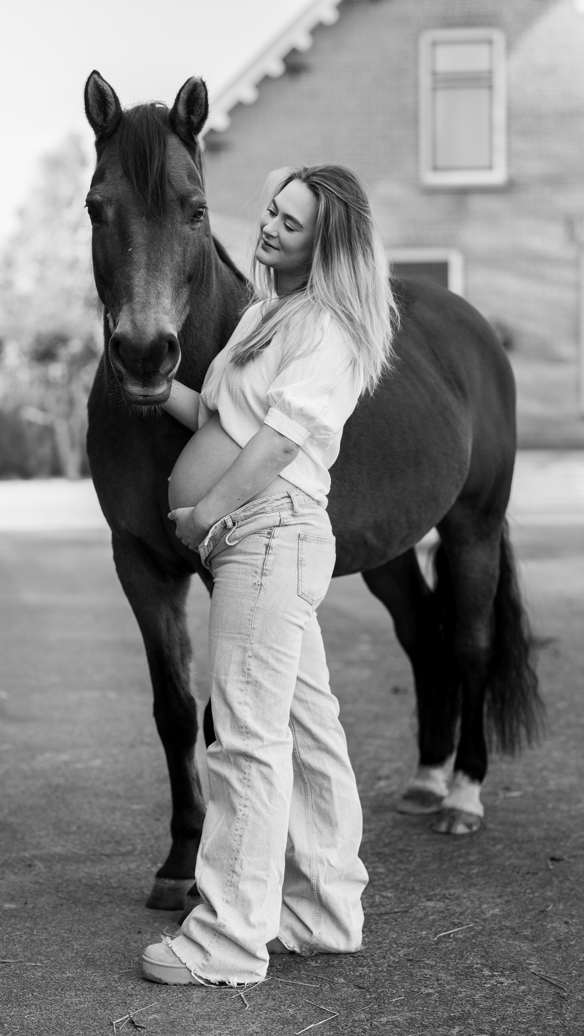 Puur Geluk Fotografie legt een zwangerschapsshoot vast in zwart-wit, waar een zwangere vrouw tijdens haar zwangerschap rustig staat naast haar paard, puur en natuurlijk gefotografeerd met aandacht voor verbinding.