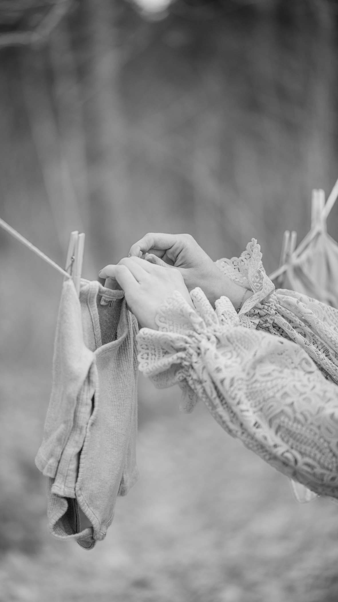 Puur Geluk Fotografie legt een ingetogen zwangerschapsdetail vast in zwart-wit, waar handen zorgvuldig babykleertjes ophangen, tijdloos gefotografeerd met aandacht voor verwachting en zachtheid.