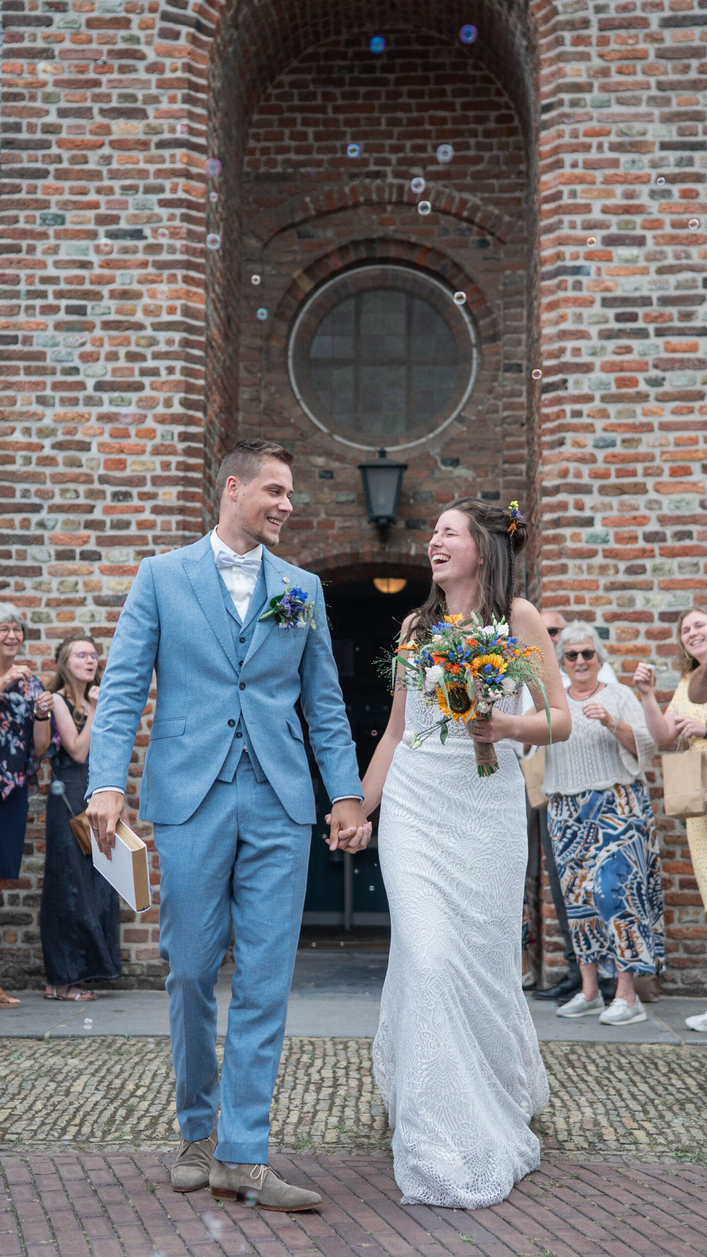Puur Geluk Fotografie legt een vrolijk moment vast na de ceremonie, waarbij het bruidspaar hand in hand de kerk verlaat, omringd door dierbaren tijdens een kleine, persoonlijke bruiloft.